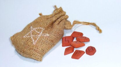 Pochettes en toile de jute contenant des runes rouges en bois, associées à des motifs mystiques sur fond clair.