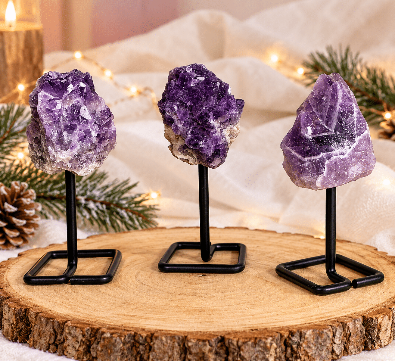 Trois pierres brutes d’améthyste violette sur socles en métal noir, présentées sur une rondelle de bois dans une décoration de Noël avec sapin et guirlandes lumineuses.